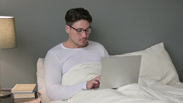 Middle Aged Man Working on Laptop in Bed  alt