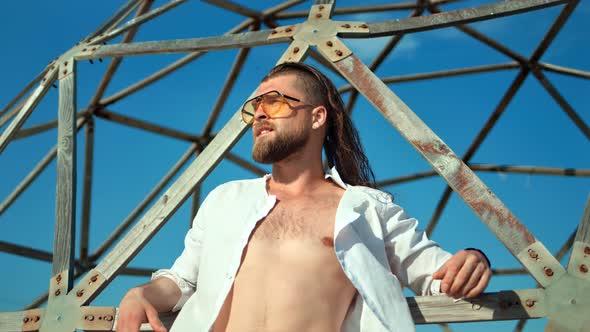 Handsome Male Fashion Model with Naked Torso Posing at Sunny Beach and Sky Background alt
