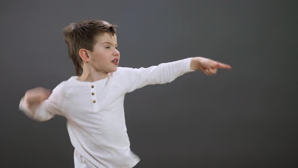 Positive Boy Pointing Aside at Empty Space on Gray Studio Background