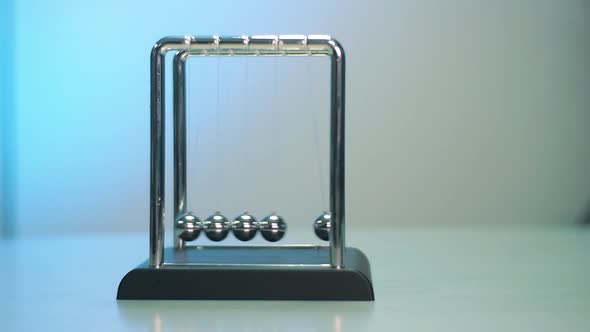 Newton's Cradle on the gray table with white and blue background. Metal balls on a thread in motion. alt