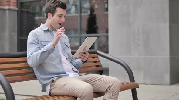 Video Chat on Tablet By Casual Young Man Sitting Outdoor alt