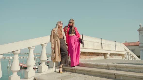 Girl Friends in Outfits Pose on Bridge Over Venetian Lagoon alt