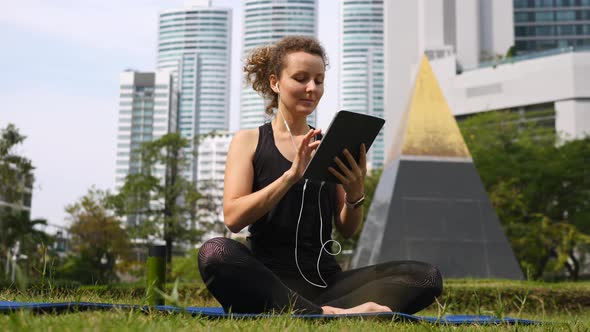 Young Woman Exercising At Park Doing Yoga Using Tablet Computer alt