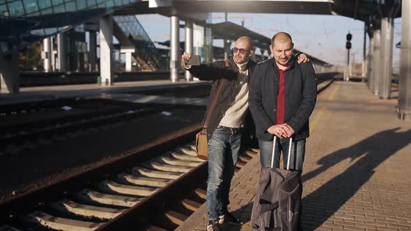 Two Men Take a Selfie on Smartphone in Anticipation of the Arrival of the Train alt