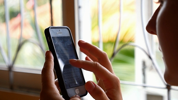 Woman Using Smartphone near Window alt