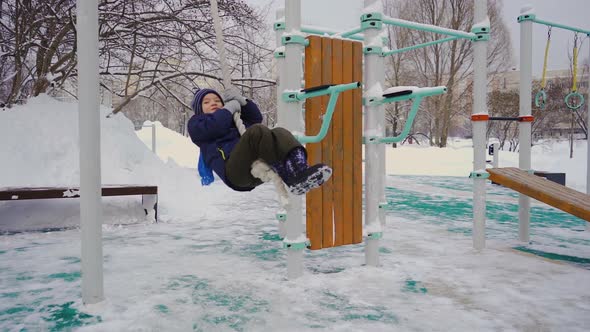 A Fiveyearold Boy Swings in the Winter on a Hanging Rope on the Playground