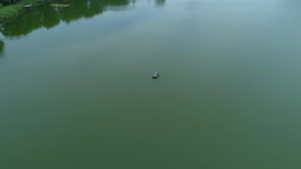 Aerial View Fisherman is Fishing Sitting on an Inflatable Boat in Middle of Lake alt