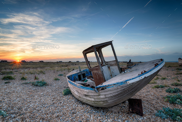 An old abandoned wooden fishing boat with nets washed up on a shingle beach