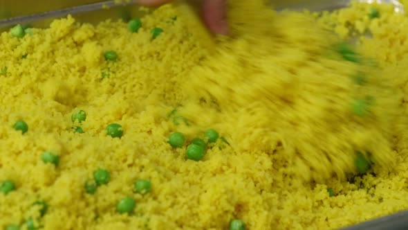 Mixing Cooked Couscous with Green Peas in a Metal Tray
