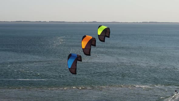 Aerial orbital reveal of a kite surfer skimming across the sea as three kites are held stationary in alt