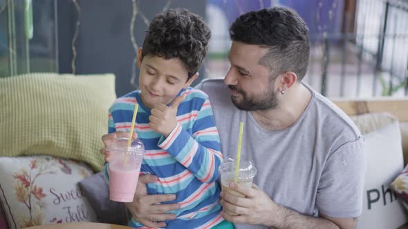 Cute Child Boy and father Drinking Milkshake with Pipette at Cafe alt