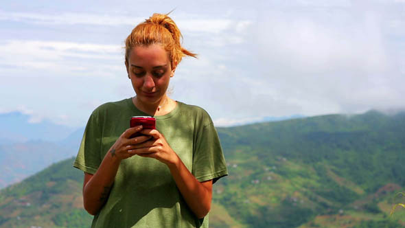 Female Tourist Text Messaging On Top Of Mountain