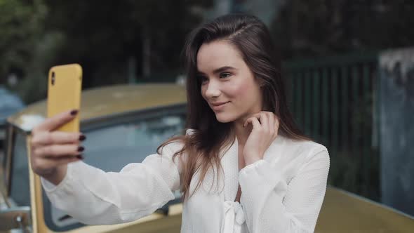 Young Woman Making Selfie on Her Smartphone. Girl Posing Smiling and Blowing a Kiss in Daytime alt