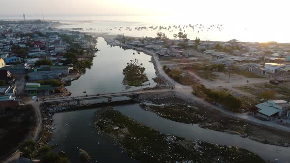 Coastal town on outskirts of Phan Rang with polluted river at sunset. Aerial alt
