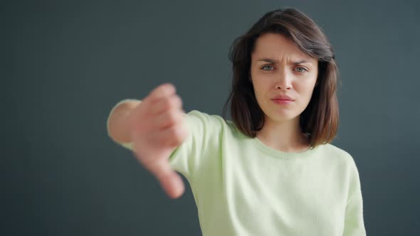 Slow Motion of Cute Girl Showing Thumbs-down Hand Gesture on Black Background alt