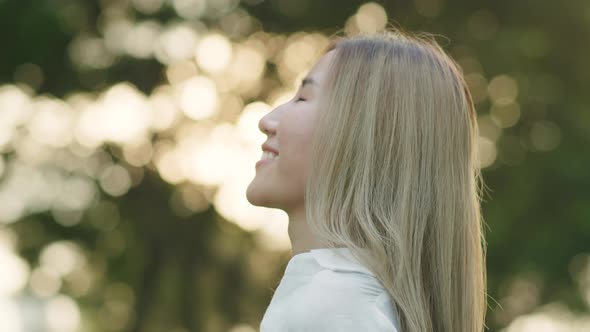 A beautiful young Asian woman closed her eyes enjoying the breeze meadow feeling happiness.