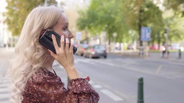 A Middleaged Caucasian Woman Talks on a Smartphone in an Urban Area  Closeup From the Side alt