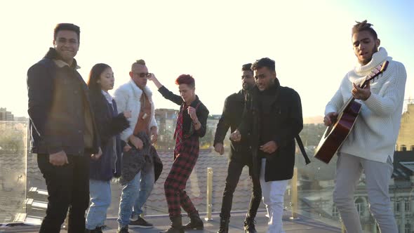 Wide Shot Group of Multiethnic People Dancing to Guitar Music on Rooftop at Sunset alt