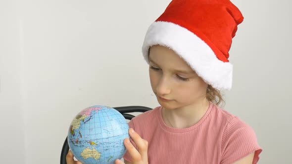 Earth Globe with Geographical Names in Ukrainian Cyrillic Letters is Held By Blond Girl in Santa Hat alt