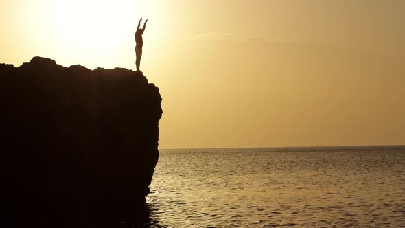 Silhouette of a man performing somersault from the cliff into the ocean alt