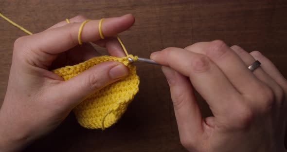 Top shot of a female holding a piece of yellow wool and a needle. Hands starting crocheting a yellow alt