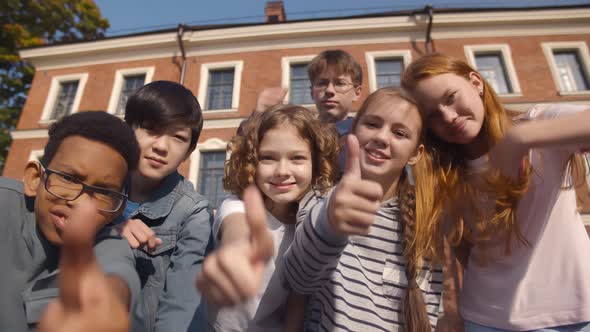 Portrait of Happy Diverse Children Looking at Camera with Thumbs Up Outdoors alt
