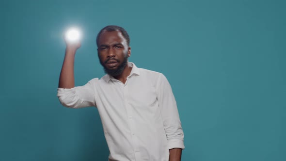 Young Man Sitting in the Dark and Holding Flashlight to See alt