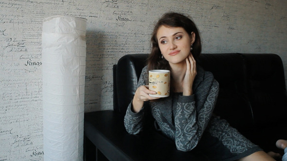 Young Woman Sitting On Sofa Drinking Tea Or Coffee