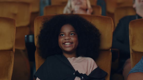 Attractive cheerful young black african girl laughing while watching film in movie theater. alt