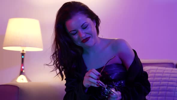 Portrait of a Sexy Brunette Woman in Round Glasses Posing Sitting on a Sofa in a Bright Room alt