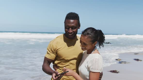 Happy african american couple taking a selfie from smartphone at the beach alt