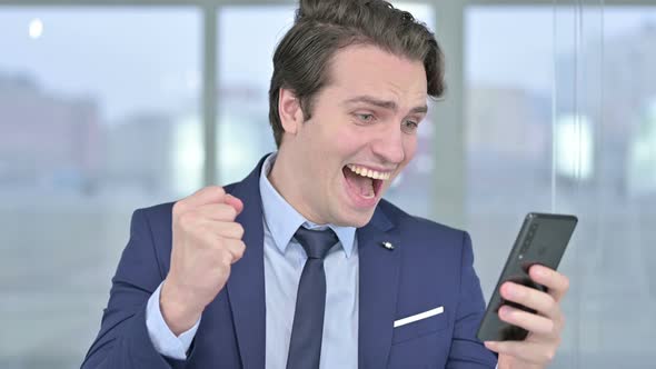 Portrait of Young Businessman Celebrating Success on Smartphone alt