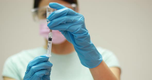 Doctor scientis in protective gloves and mask holding glass vial with injection liquid. Vaccination