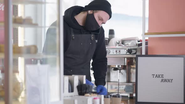 Concentrated Barista Talking on the Phone Putting Drinking Straws in Take Away Disposable Coffee alt