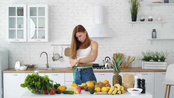 Young athletic girl measures her waist near a table with healthy food alt