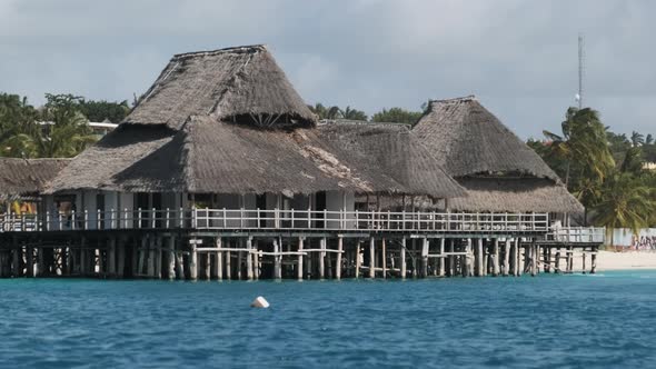 African Restaurant with Thatched Roof on Wooden Poles Above the Ocean alt