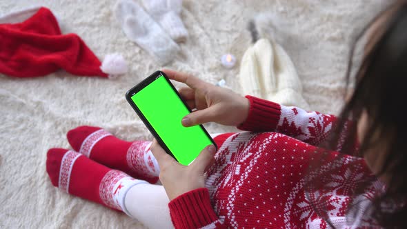 Brunette Woman Is Sitting on a Fluffy Blanket Uses Mobile Phone with Green Screen for Copy Space