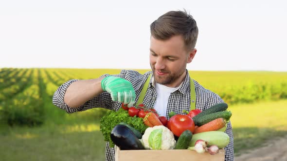 Young Farmer is Holding a Box of Organic Vegetables and Look at Camera alt
