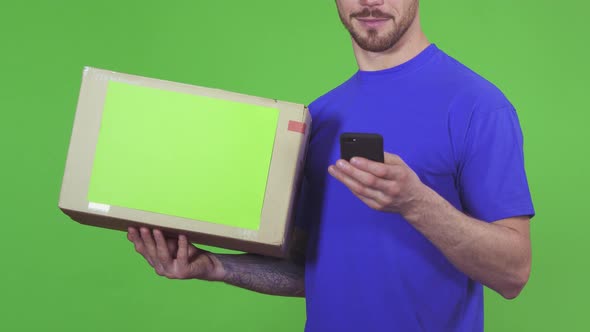 Cropped Shot of a Deliveryman with a Package Texting His Client Using Smart Phone alt