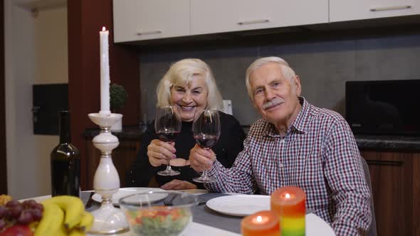 Senior Relaxed Couple Eating Dinner and Drinking Glasses of Red Wine Together in the Kitchen at Home alt