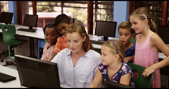 Teacher assisting school kids on personal computer in classroom alt