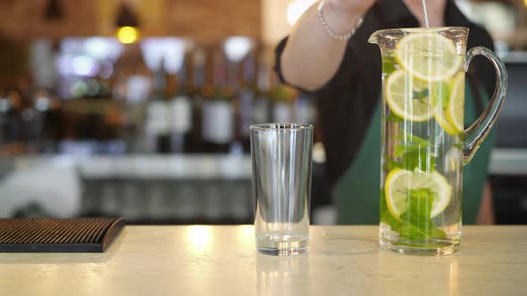 Bartender Hand Stiring a Tall Glass with Lemon Mint Water Beside an Empty Glass in Bar
