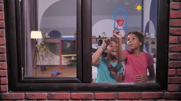 Happy Mixed Race Sisters Painting on Window Pane alt
