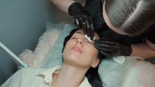 Eyelash Extension Master Degreases the Client's Eyelashes with Cotton Pads with a Solution alt
