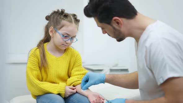Portrait of Concentrated Scared Girl Sitting on Medical Couch As Blurred Doctor Disinfecting Hand alt