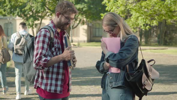 Shy Boy and Girl in Eyeglasses Standing in University Campus Yard and Talking. Side View Portrait of alt