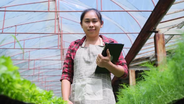 Beautiful gardener woman uses a tablet while working in a greenhouse. alt
