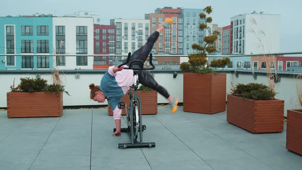 Athletic Girl Make Acrobatic Trick on Bike Exercising Workout on Stationary Cycling Machine Outdoors alt