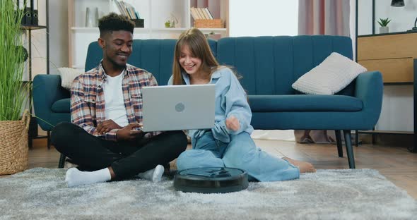 Multiethnic Couple which Watching Interesting Video on Laptop on the floor alt
