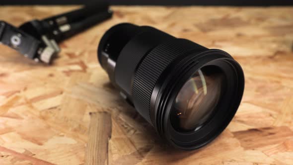 Close up Of Camera Lens With Tripod On Wooden Table. alt